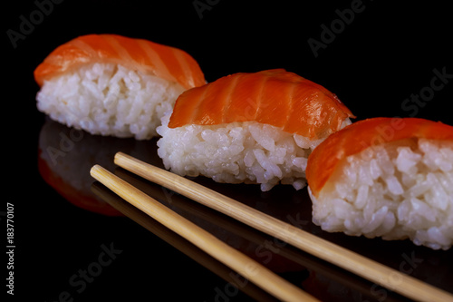 Salmon sushi nigiri chopsticks over black background