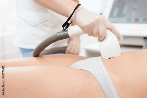 The woman came to the procedure of laser hair removal. The doctor treats her stomach with a device.