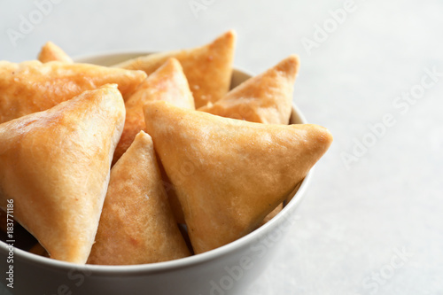 Bowl with delicious samosas on light background