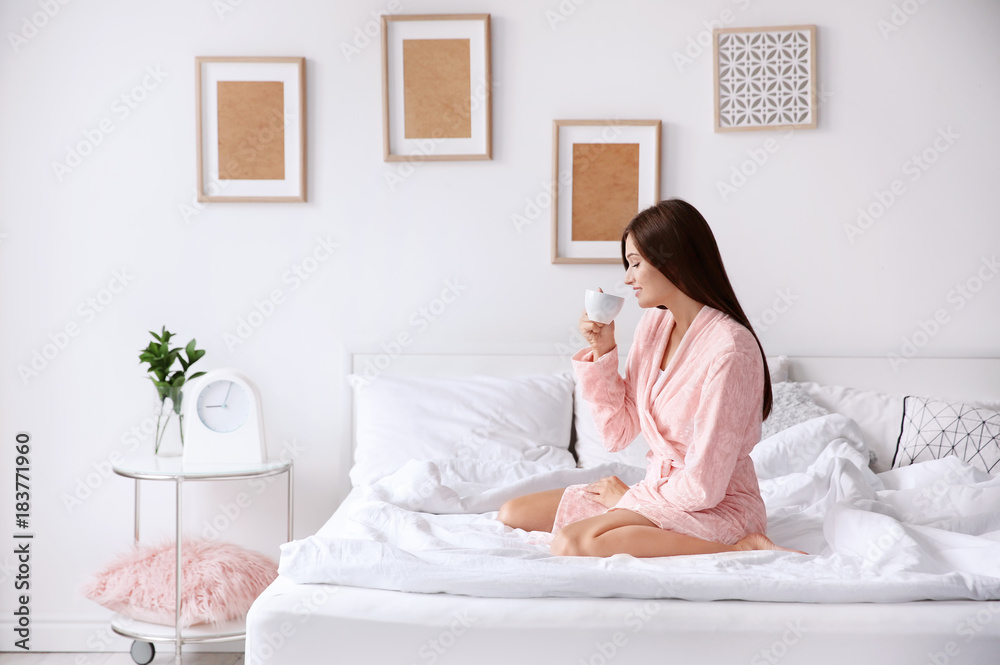 Young woman drinking coffee while sitting on bed at home Young woman drinking coffee while sitting on bed at home