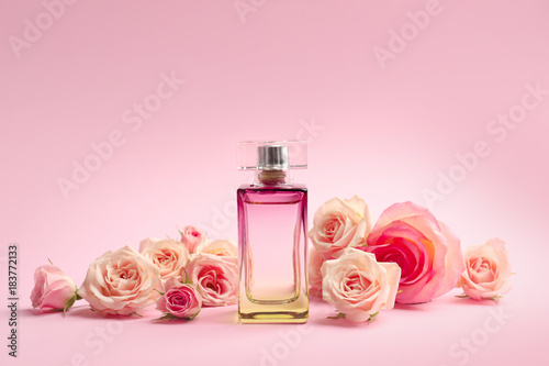 Bottle of perfume with flowers on color background