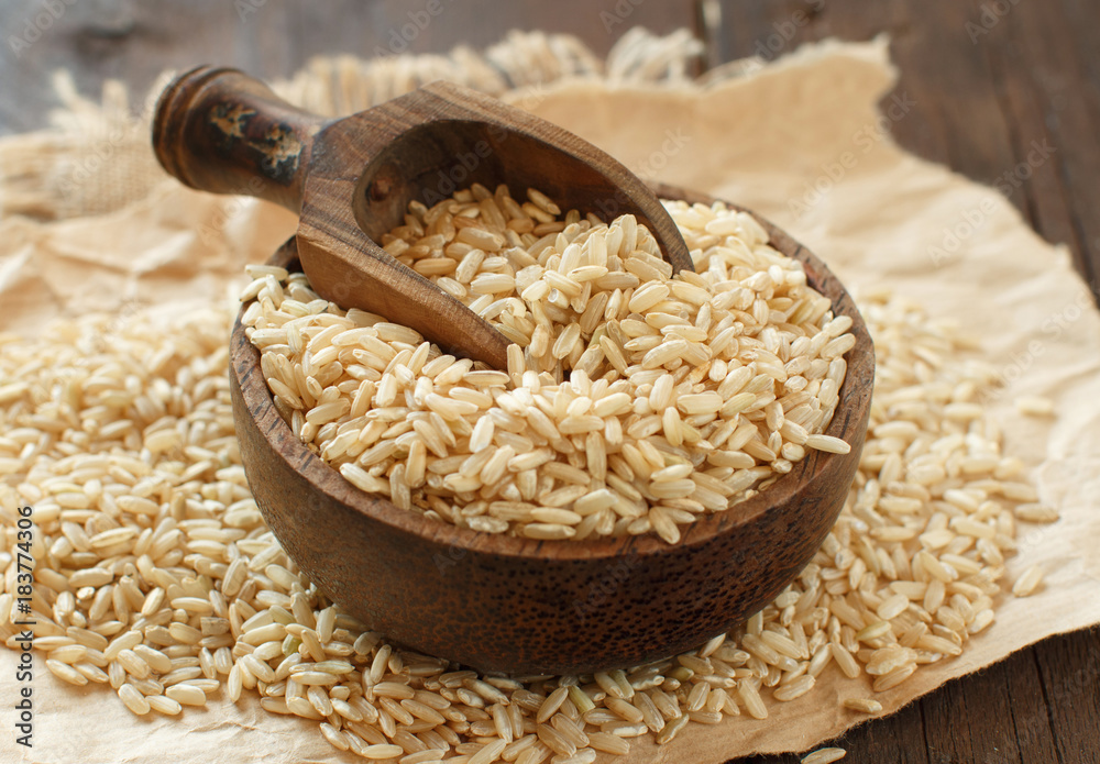 Pile of Brown rice in a bowl with a wooden spoon - obrazy, fototapety, plakaty 