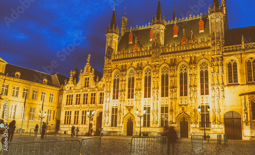 BRUGES, BELGIUM - MARCH 2015: Tourists visit ancient medieval Burg Square at night. Brugge attracts more than 2 million people annually