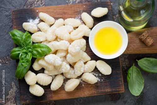 Top view of raw potato gnocchi with olive oil and green basil on a rustic wooden chopping board, horizontal shot