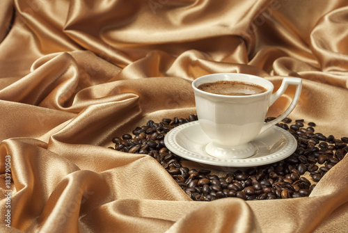 a cup of coffee and coffee beans on satin fabric