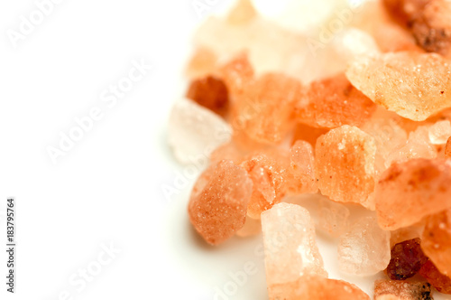 Macro crystals of orange and pink himalayan rock salt on white background