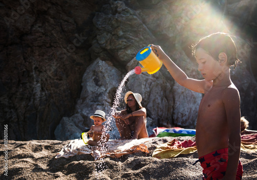 Boy on beach sprinkling toy watering can, Begur, Catalonia, Spain photo