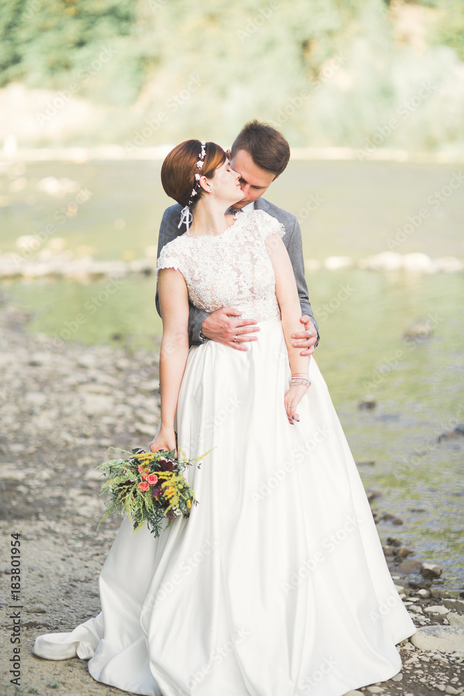 Bride and groom holding beautiful wedding bouquet. Posing near river Bride and groom holding beautiful wedding bouquet. Posing near river