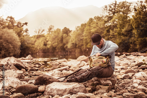 Fisherman sitting on river rocks searching fishing bag, Mozirje, Brezovica, Slovenia photo