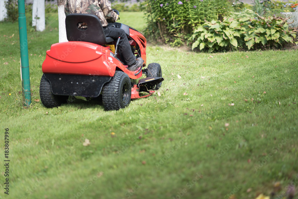 Gardener driving a riding lawn mower in a garden Gardener driving a riding lawn mower in a garden