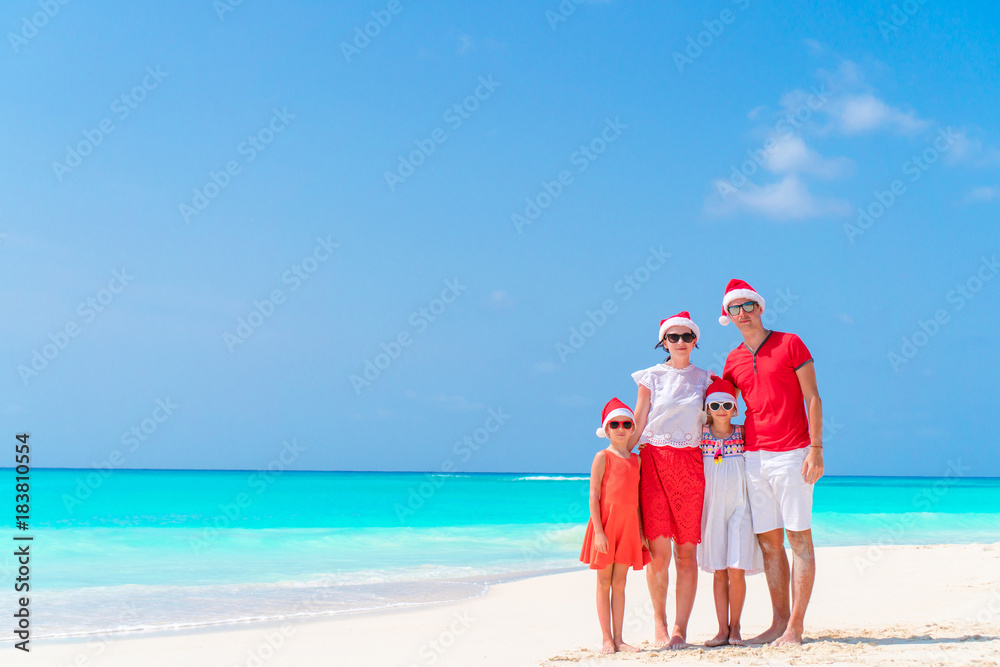 Happy family in red Santa hats on a tropical beach celebrating Christmas vacation