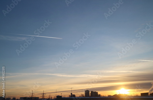 Cirrus clouds in the autumn sky in the evening at sunset, trail from the plane, evening over the industrial zone