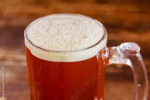 Close up of glass of beer with foam on a wooden table in a dark pub