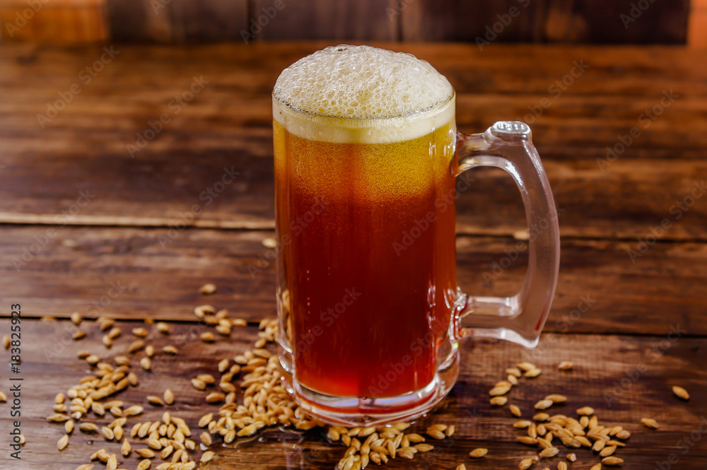 Indoor view of glass of beer with wheat in the base on a wooden table on a blurred background Indoor view of glass of beer with wheat in the base on a wooden table on a blurred background