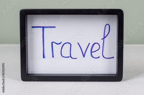 Text word TRAVEL, in black frame, on white table.