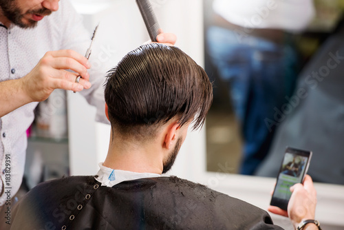 Man using smartphone while having his hair cut in hairdressing salon
