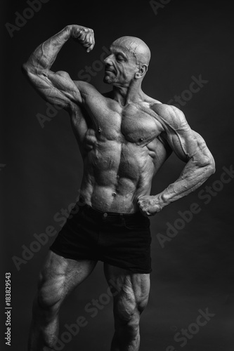 Professional strong bodybuilder athletic man posing front biceps in studio