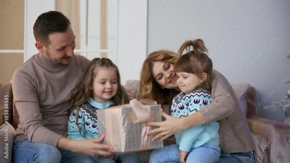 Happy family at Christmas, mum, dad and two little girls sitting at home on the sofa near the Christmas tree to open the gifts. Happy family at Christmas, mum, dad and two little girls sitting at home on the sofa near the Christmas tree to open the gifts.