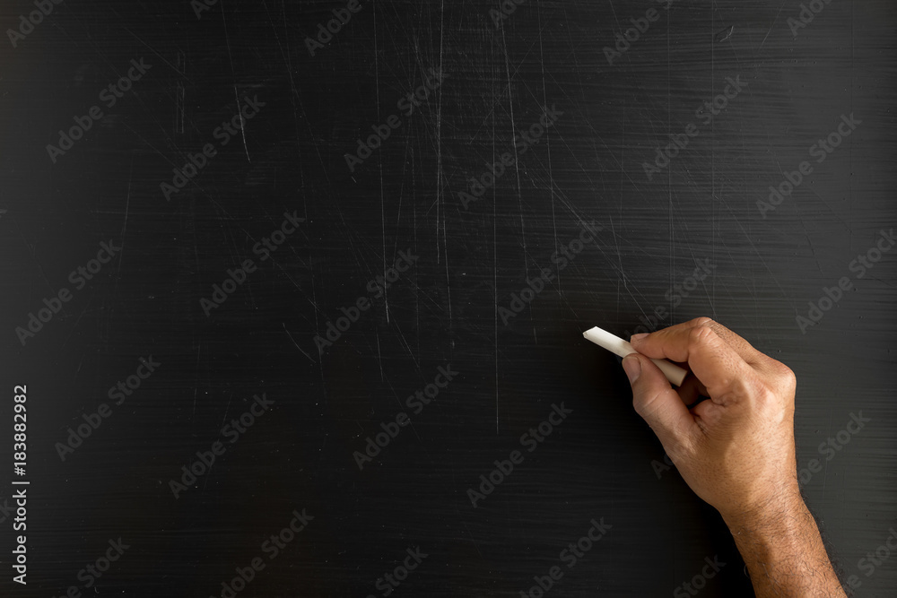 Naklejka premium Hand holding a chalk and writing something against blackboard with copy space on blackboard