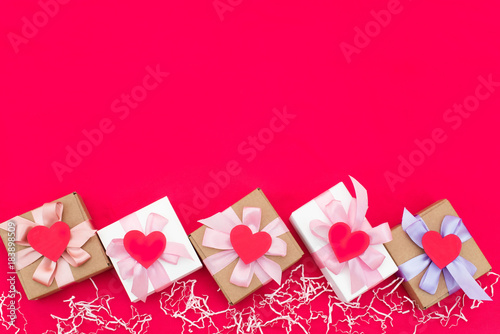 Five gift boxes tied with satin coloured ribbon on a red background a Red heart.