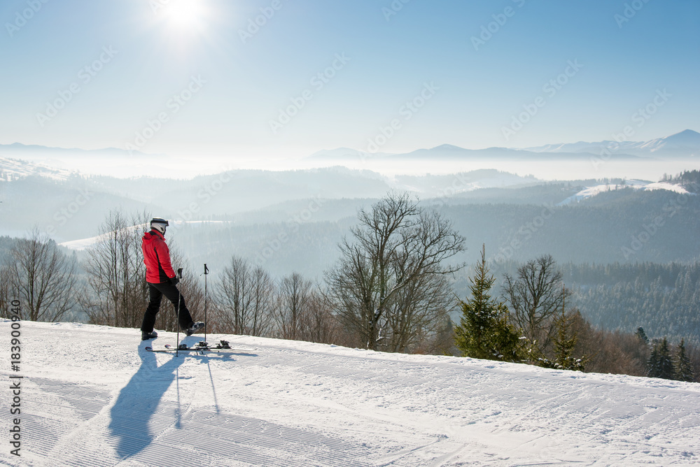 Rearview shot of a male skier resting after the ride standing on top of the ski slope looking around enjoying breathtaking view of snowy mountains on a sunny winter day