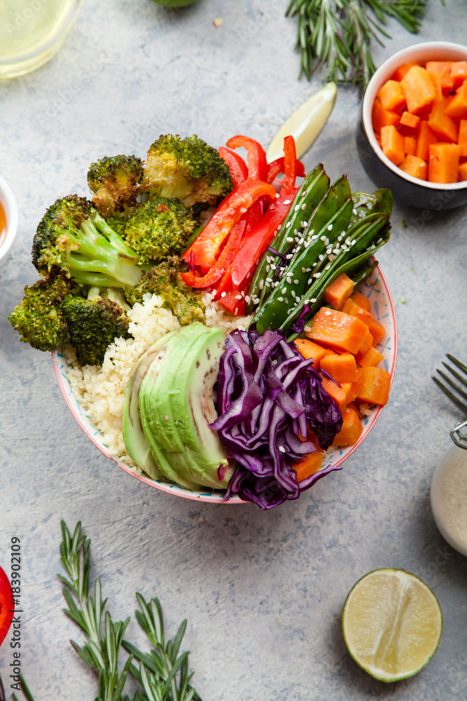 Tasty healthy bowl for lunch with couscous, baked broccoli and carrots cut in cubes, fried peas, avocados and red cabbage. Easy vegetarian diet concept. Rustic background. Top view.