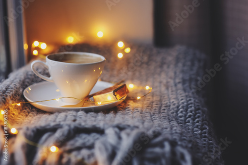 cozy winter or autumn morning at home. Hot coffee with gold metallic spoon, warm blanket, garland and candle lights, swedish hygge concept. photo