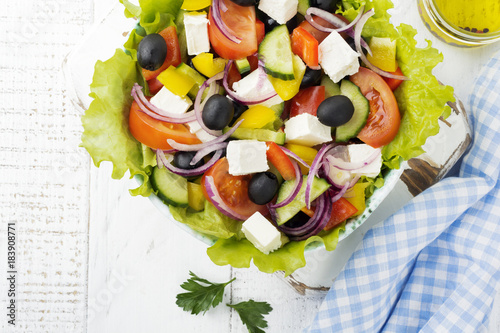 Greek salad in a ceramic plate on a white wooden background. Traditional Greek dish. Selective focus.Top view. photo