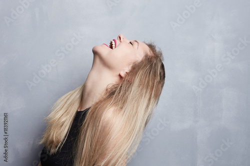 People, youth, joy, fun, happiness and relaxation concept. Indoor portrait of trendy-looking hipster female with long blond hair and pink lips smiling cheerfully,laughing while watching good comedy.