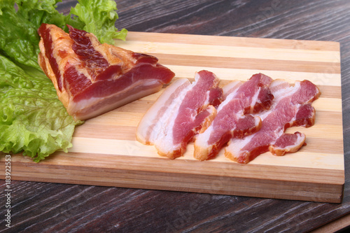 Fresh homemade smoked bacon with leaves lettuce on a wooden cutting board. Selective focus. photo