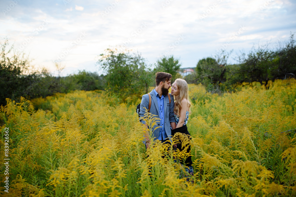 Young couple in love dressed in country style standing on field of flowers