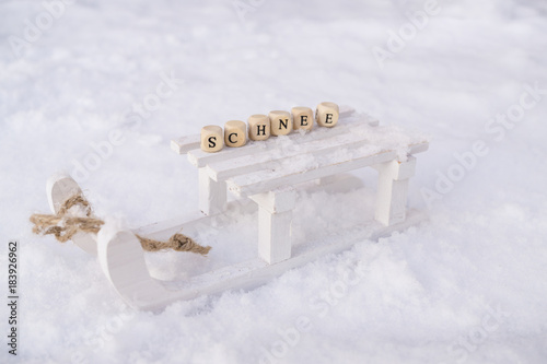 Ein weißer Holzschlitten im Schnee mit dem Wort Schnee in Buchstabenwürfeln