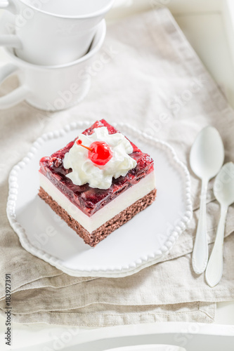 Delicious jelly cherry cake with cream on white plate