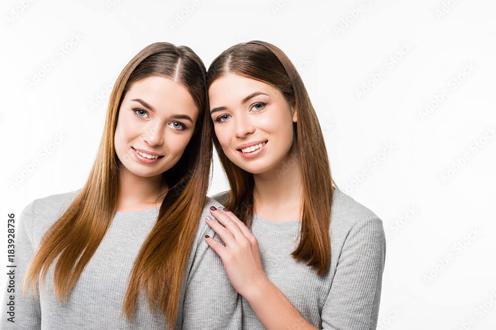 portrait of young smiling twins leaning on each other and looking at camera isolated on white