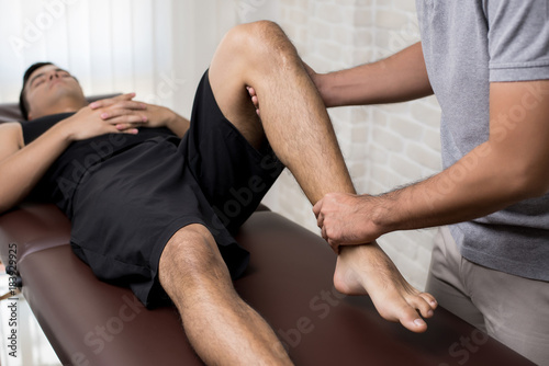 Therapist treating injured leg of athlete male patient in clinic