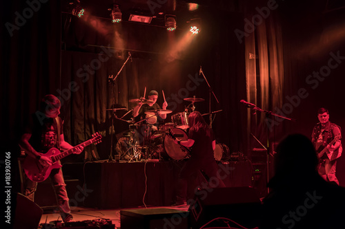 Photography Drummer and three guitarists at a concert with red lights, in the smoke