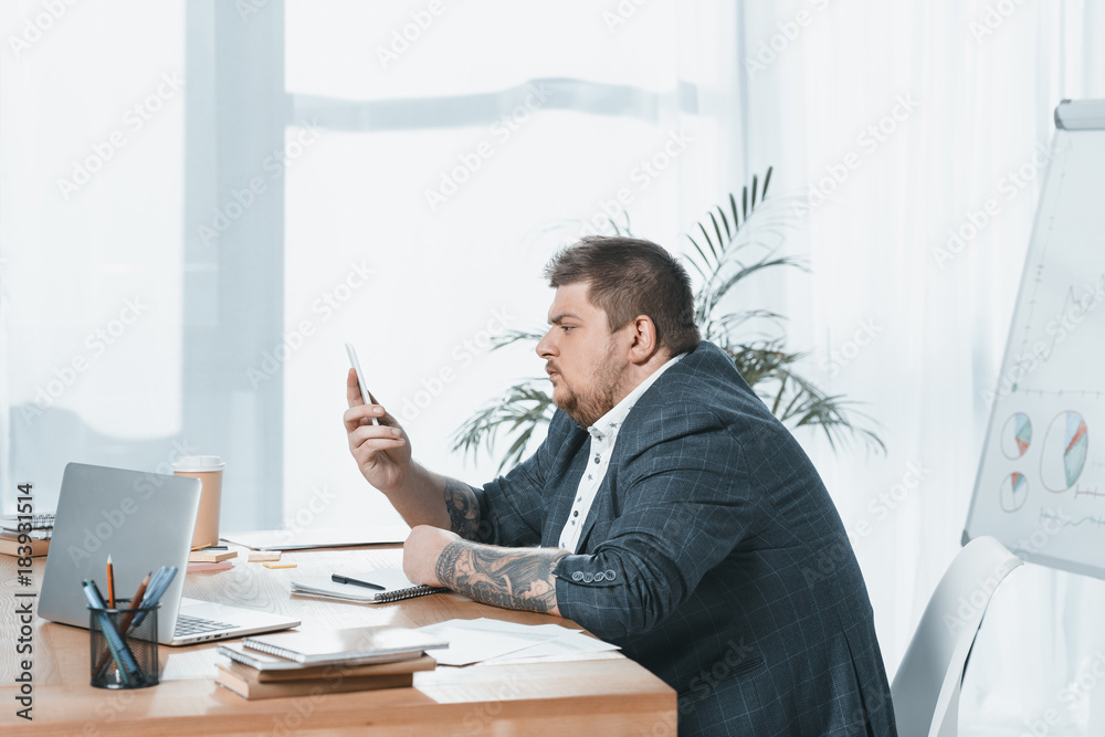 overweight businessman in suit working with smartphone and laptop at workplace overweight businessman in suit working with smartphone and laptop at workplace