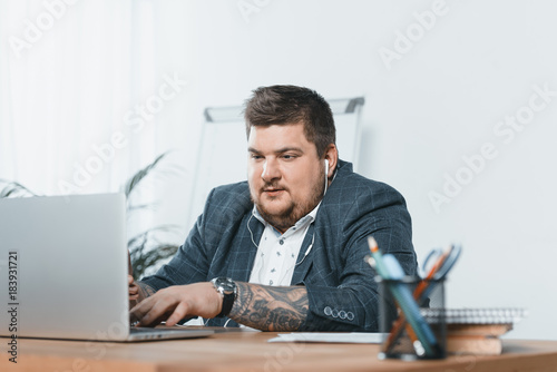 Foto overweight businessman listening music with earphones while working on laptop in