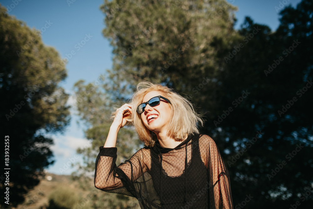 Woman in sunglasses laughs while touch her hair happy in nature.
