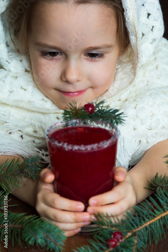 .A girl in a white knitted scarf holds a cup of cranberry mors