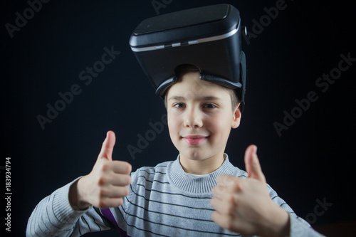 close-up happy boy shows thump up using a virtual reality helmet. Child getting experience in using VR 360 photo