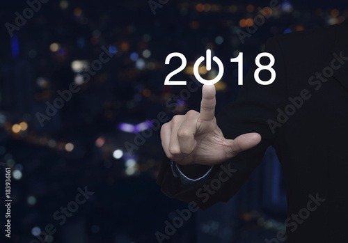 Businessman pressing 2018 start up business icon over blur colorful night light city tower, Happy new year concept