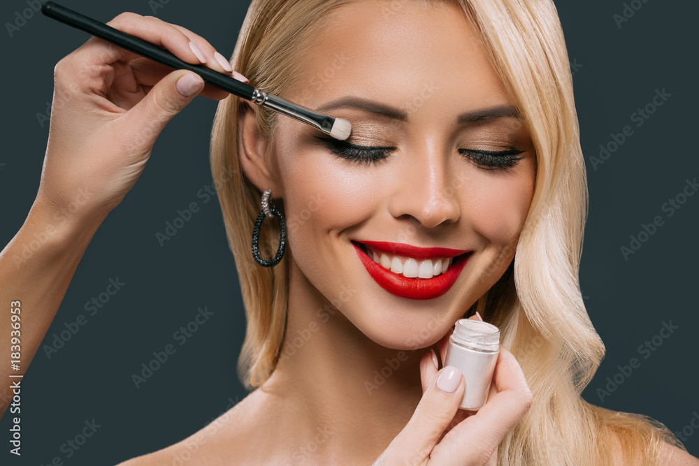beautiful blonde woman applying glamorous makeup with eyeshadows, isolated on grey beautiful blonde woman applying glamorous makeup with eyeshadows, isolated on grey
