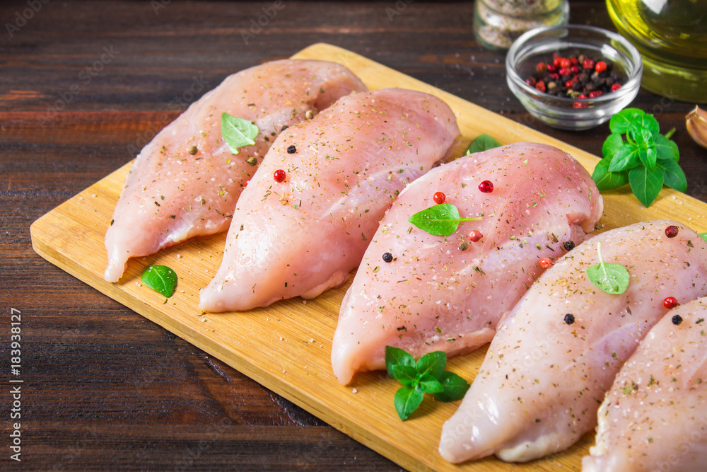 Raw chicken fillets on a cutting board against the background of a wooden table. Meat ingredients for cooking. Raw chicken fillets on a cutting board against the background of a wooden table. Meat ingredients for cooking.