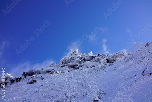 厳冬期の八ヶ岳。冷たい北風が吹き付け、氷で覆われた険しい岩稜を行く登山者