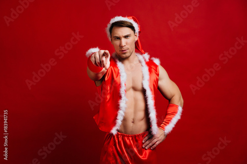 christmas holidays. sexy strong santa claus wearing hat. Young muscular man. red background.