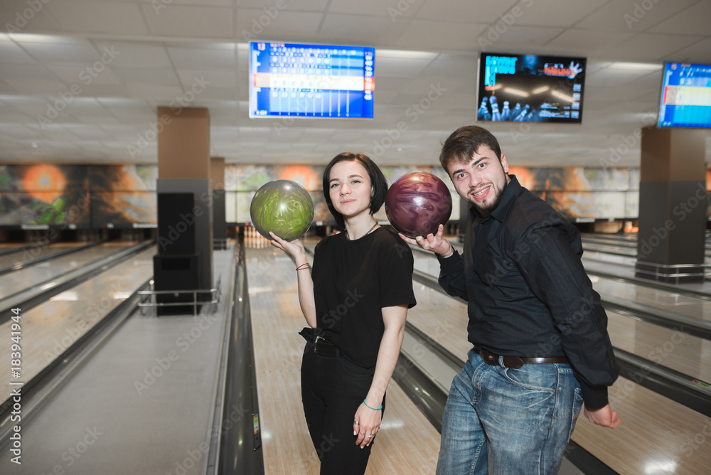 Two fun young people with bowling balls in their hands are standing on the  background of the track. A couple playing bowling. Stock Photo | Adobe Stock