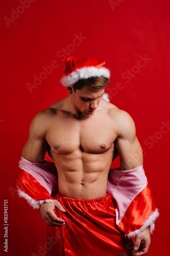 christmas holidays. sexy strong santa claus wearing hat. Young muscular man. red background.