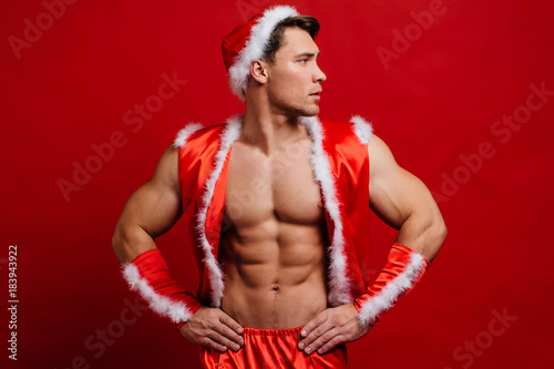 christmas holidays. sexy strong santa claus wearing hat. Young muscular man. red background.