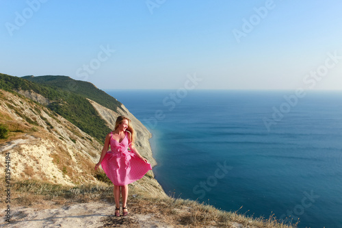 A girl in a pink dress jumps on the seashore and smiles. The joy of travel. Healthy lifestyle. Happiness and smile.